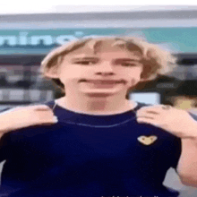 a young man in a blue shirt is making a funny face in front of a store .