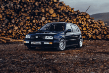 a black car with a license plate that says sr95242 is parked in front of a pile of logs