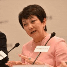 a woman in a pink shirt is sitting at a podium speaking into a microphone .