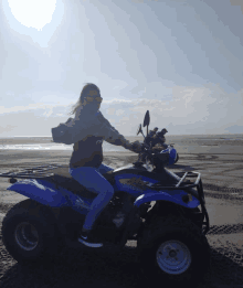 a woman is riding a blue atv on a sandy beach