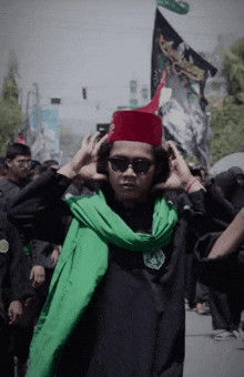 a man wearing sunglasses and a red hat stands in front of a flag that says ' muhammad ' on it