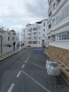 a row of white buildings along a street with bags on the sidewalk