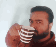 a man with a beard is drinking from a striped coffee cup