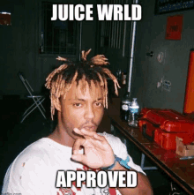 a man with dreadlocks is sitting at a table with his hand on his chin and the words `` juice wrld approved '' .