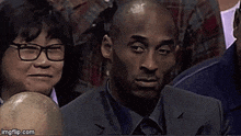 a man in a suit and tie is sitting in a stadium with a woman behind him .