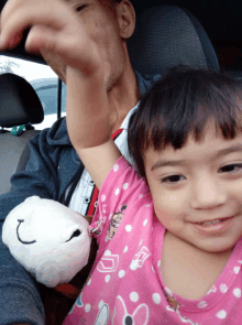 a little girl in a pink minnie mouse outfit is sitting on a man 's lap in a car