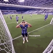 a soccer player is making a heart shape with his hands while standing in front of a goal net .