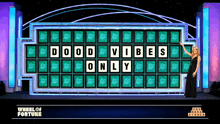 a woman stands in front of a wheel of fortune board that reads good vibes only