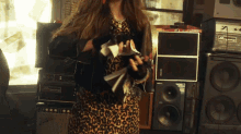 a woman in a leopard print dress is standing in front of a stack of speakers and a stack of amps