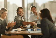 a group of people sitting around a table shaking hands and clapping