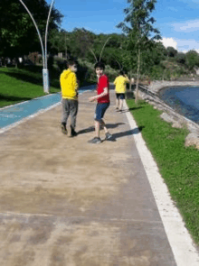 a group of young boys are walking down a path next to a body of water .