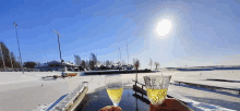 a person is holding two glasses of wine in front of a snowy dock