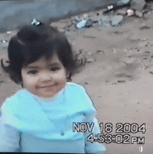 a little girl is smiling and wearing a blue shirt with the date nov 18 2004 on it