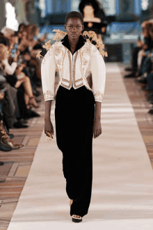 a model walks the runway at a fashion show wearing a white jacket and black pants