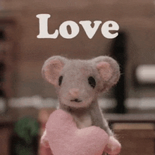 a stuffed mouse is holding a pink heart and the word love is above it