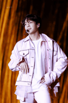 a young man wearing a pink jacket and white shirt stands on stage with his hands on his hips