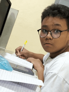 a boy wearing glasses is writing in a notebook with a yellow marker