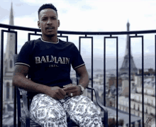 a man wearing a balmain t-shirt sits on a balcony