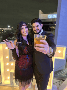 a man and a woman are posing for a picture and the man is holding a glass of beer