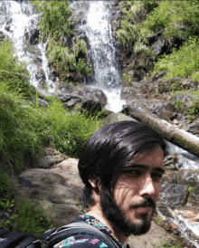 a man standing in front of a waterfall with a backpack