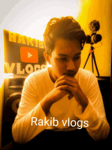 a man sitting in front of a sign that says rakib vlogs