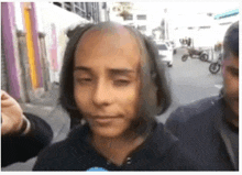 a man with a very short haircut is standing on a street with other people