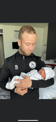 a man holding a baby wearing a shirt with the letter r on the front