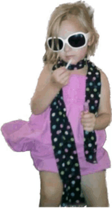 a little girl wearing sunglasses and a scarf holds a lollipop