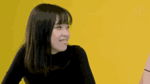 a woman in a black shirt is smiling in front of a yellow wall .