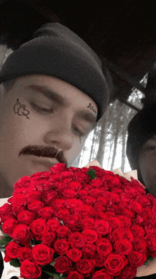 a man with a tattoo on his face has a bouquet of red roses in front of him