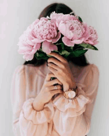 a woman is holding a bouquet of pink flowers covering her face .