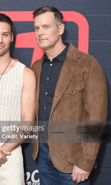 a man in a brown jacket stands next to another man