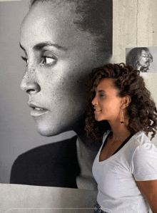 a woman standing in front of a large black and white photo of a woman 's face