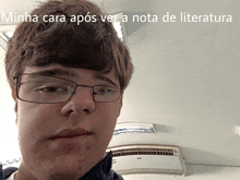 a young man wearing glasses looks at the camera with the caption minha cara apos ver a nota de literatura