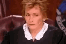 a woman is sitting in a chair in a courtroom wearing a black sweater and white collar .