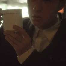 a man in a suit and tie holds a white cup in his hand