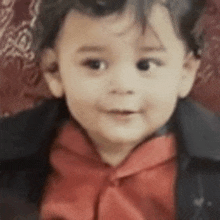 a little boy wearing a red bow tie and a black jacket is looking at the camera .