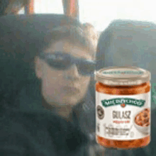 a man wearing sunglasses is sitting in a car next to a jar of salsa .