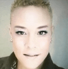 a close up of a woman 's face with a shaved head and a black jacket .