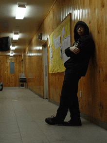 a person leaning against a wooden wall with a bulletin board behind them