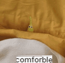 a stuffed green worm is sitting on top of a yellow blanket on a bed .