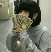 a girl is holding a fan of money in front of her face ..