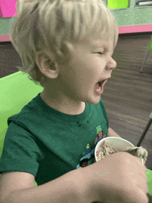 a young boy wearing a green shirt is eating ice cream from a cup