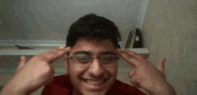 a young man wearing glasses is pointing at his head