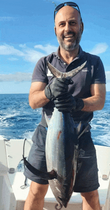 a man on a boat holding a large fish that says nautica on his shirt