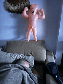 a pink inflatable man is standing on a couch next to a sleeping man