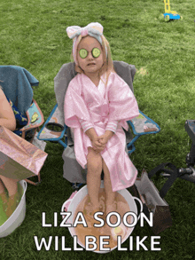 a little girl wearing a pink robe and cucumber slices on her eyes is sitting in a chair