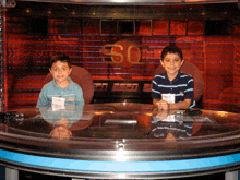 two young boys sit at a table in front of a sign that says so