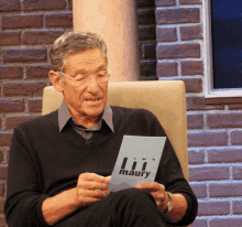 a man sitting in a chair holding a piece of paper that says maury on it