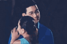 a woman in a blue dress is kissing a man in a blue shirt .